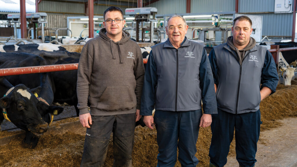 Three men standing in a milking parlour