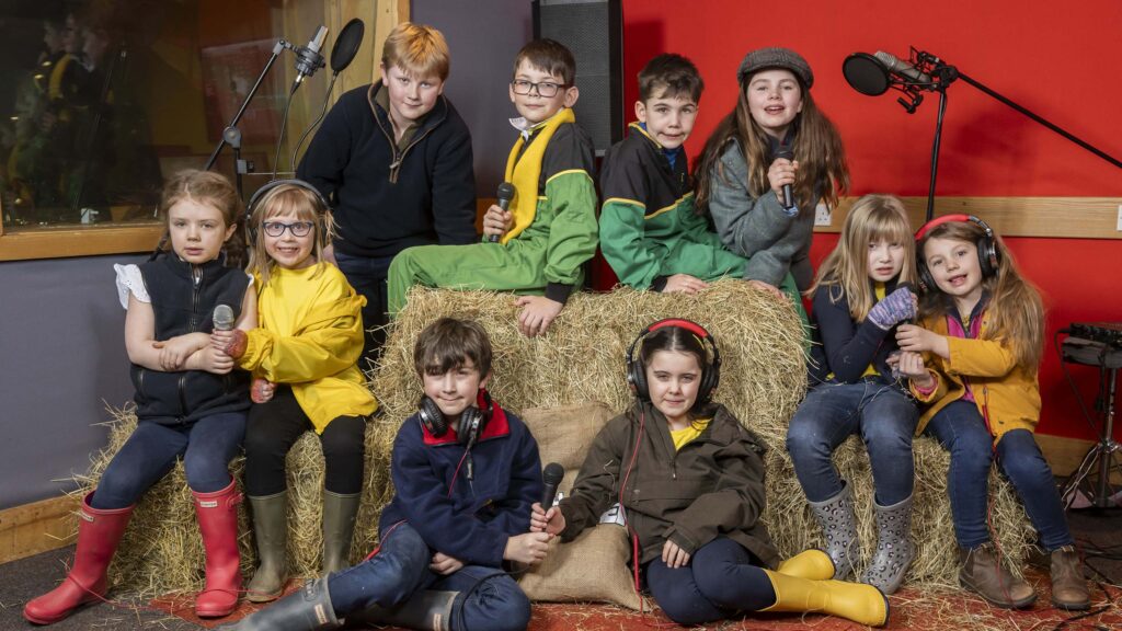 Group of children holding microphones sitting on a bale