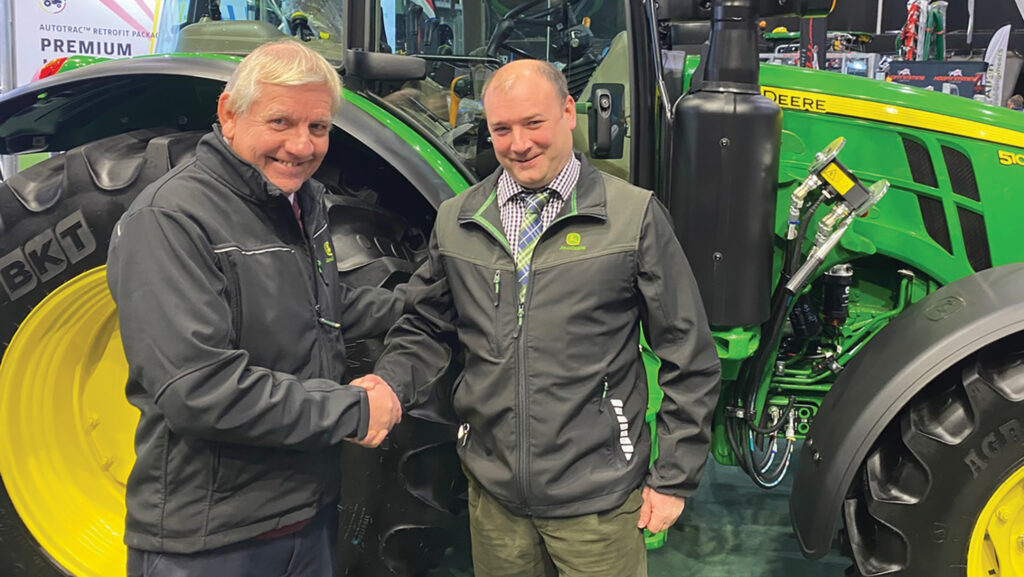 Two men shake hands in front of tractors