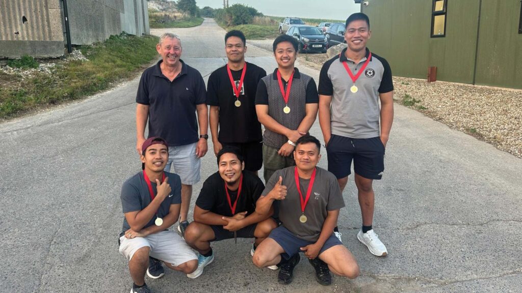 Group of men posing with medals in a farmyard