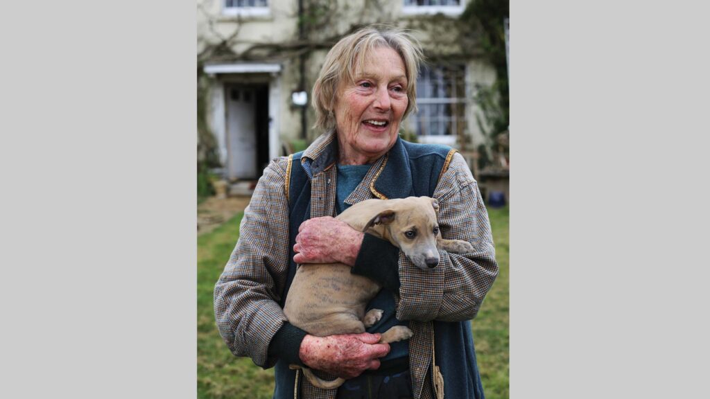 Woman holding a puppy in front of farmhouse
