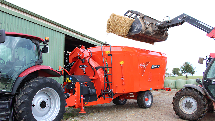 Copilot said: CopilotRed tractor and orange feed mixer beside green barn; loader lifts hay bale above mixer in farmyard setting.