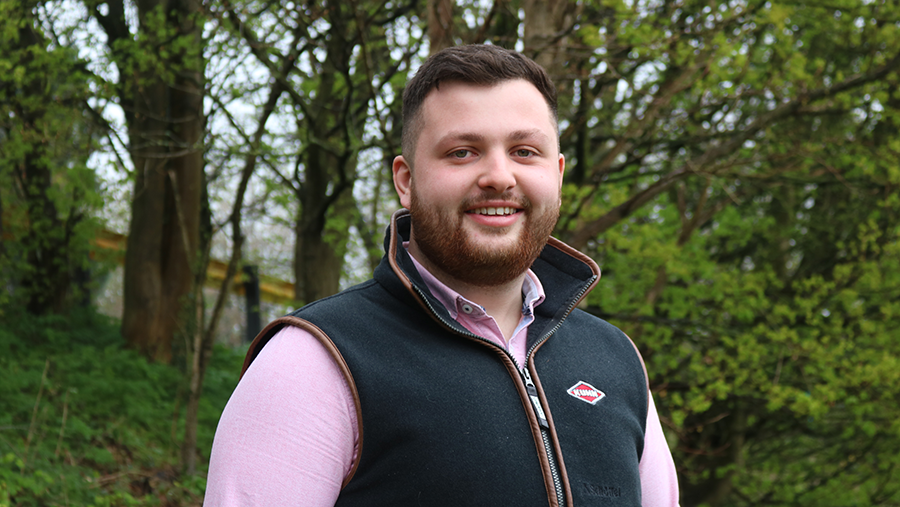 Rhodri Jenkins wearing a shirt and dark vest, standing in front of green woodland foliage.