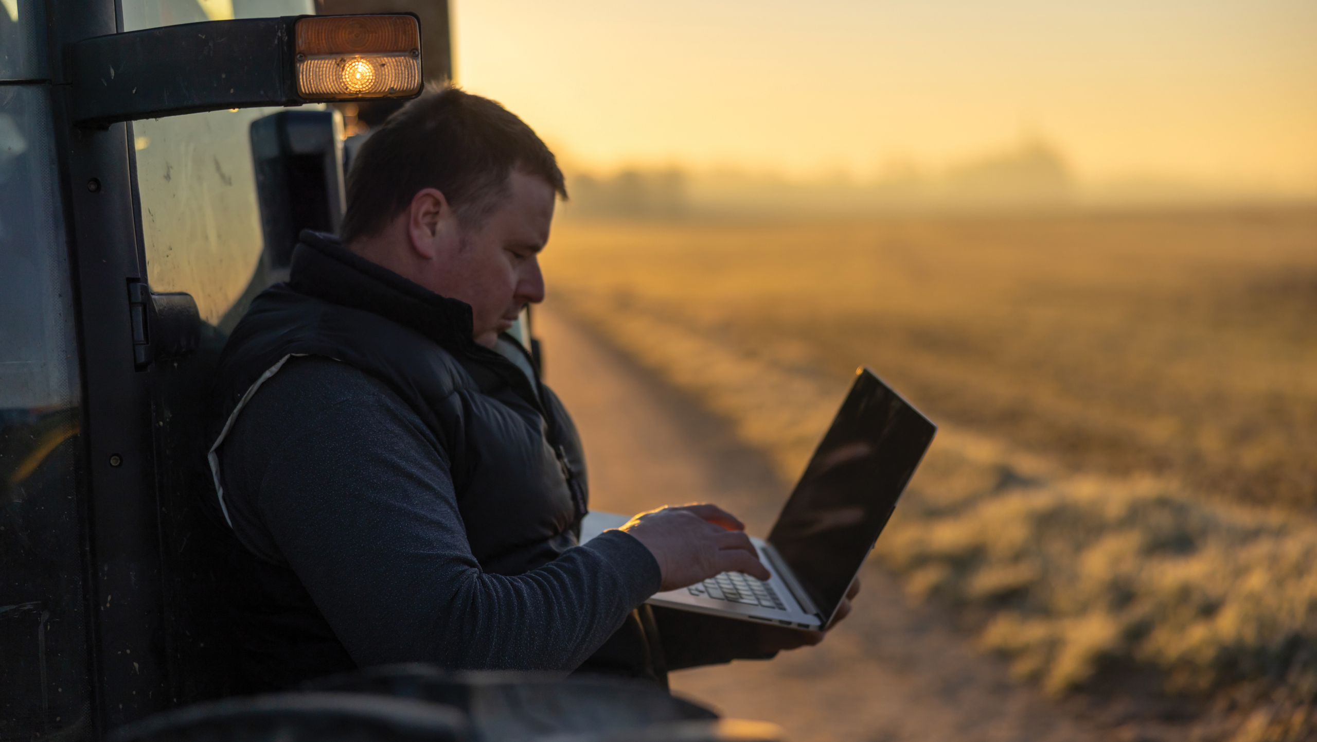 Silhouette of a farmer looking at a laptop in the sunset