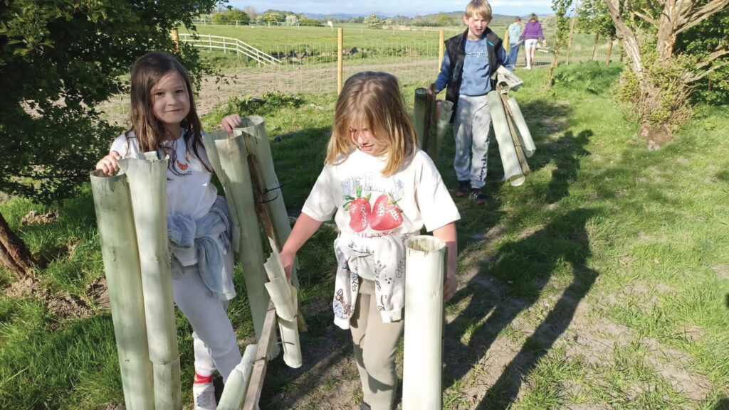Three children carrying plastic tree protectors