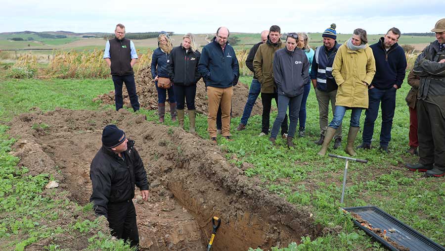 Person stood in dug hole, talking to group of people