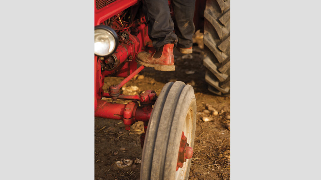 Close-up of wheel and farmer stepping into tractor