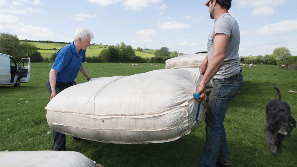 Farmers lifting bag of wool