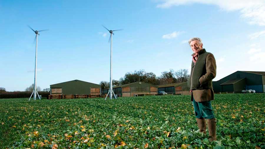 Man stood in arable field with wind turbine in background