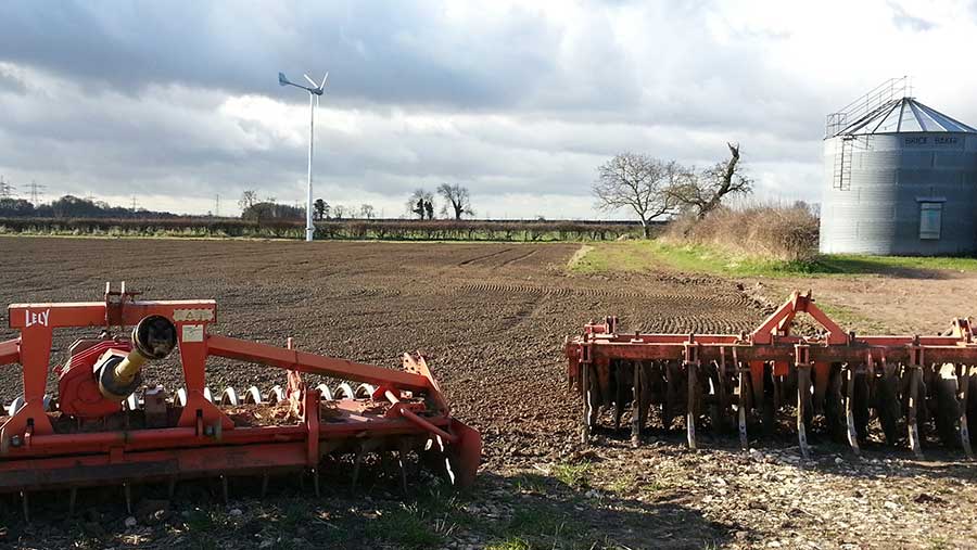 Farm machinery in arable field with wind turbines in background