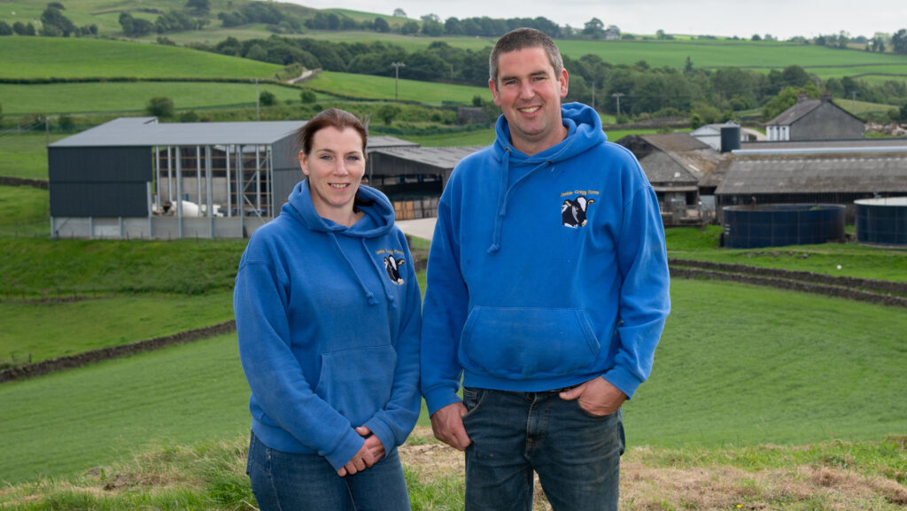 Couple stand in front of farm buildings