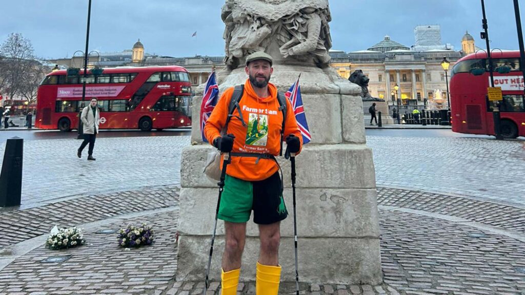 Man in walking gear poses in front of a monument