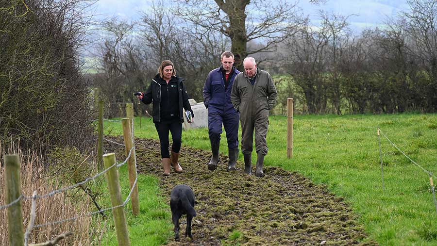 Three people walking on farm path with dog in foreground