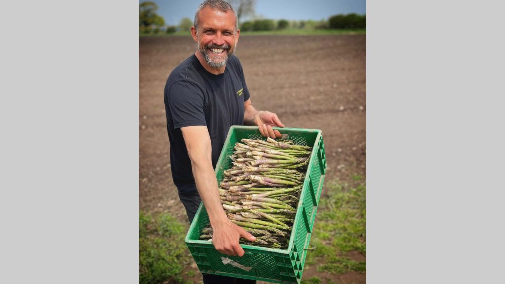 Farmer smiles holding a box of asparagus