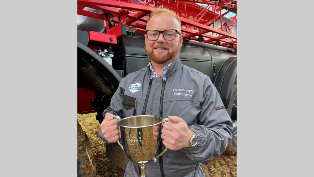 Farmer holds silver trophy in front of a sprayer