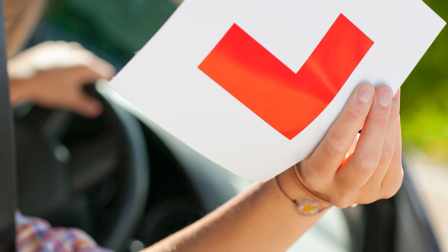 Young woman in car holding up L sticker