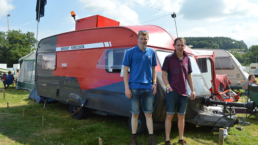 A Massey-themed caravan. Two men stand beside it.