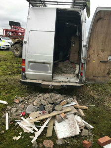 Building rubble sits outside a van with its back door open