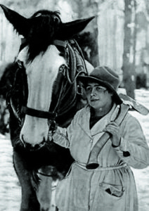 A woman, who is carrying an axe, leads a horse. 