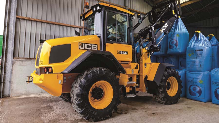 A yellow loader moving large blue bags in a barn