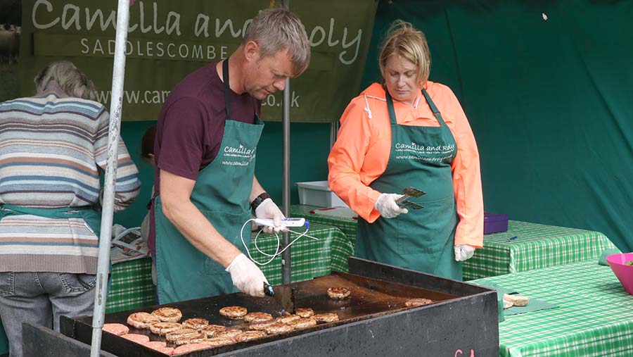 A man and a woman cook burgers for sale outside 