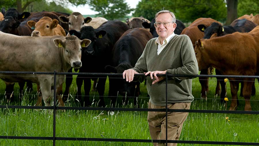 Sir Ken Morrison standing in a field with cows behind him