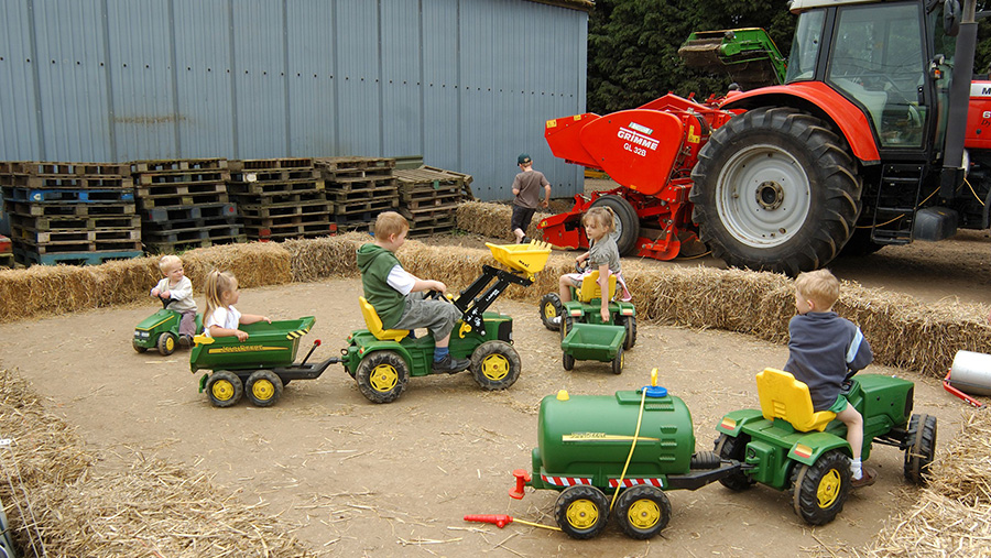 Children riding toy tractors on a farm