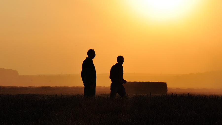 Silhouette of two farmers in a field at sunset