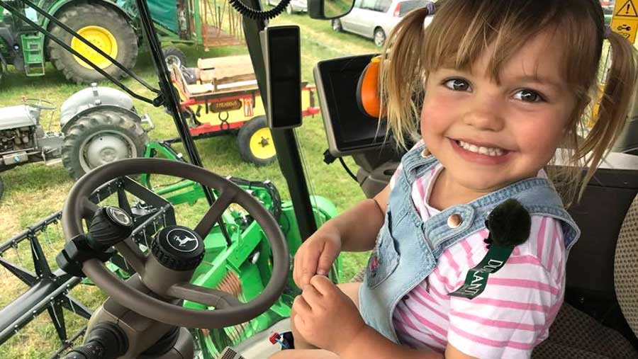 A young girl smiles as she sits in a tractor cab